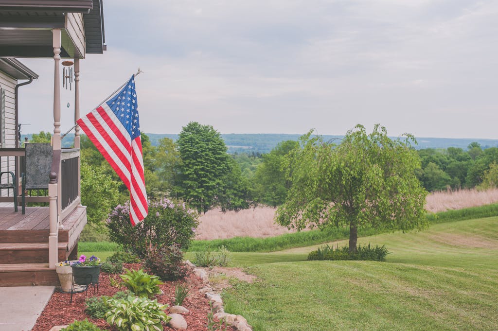 A serene suburban house porch displaying an American flag with a scenic background.